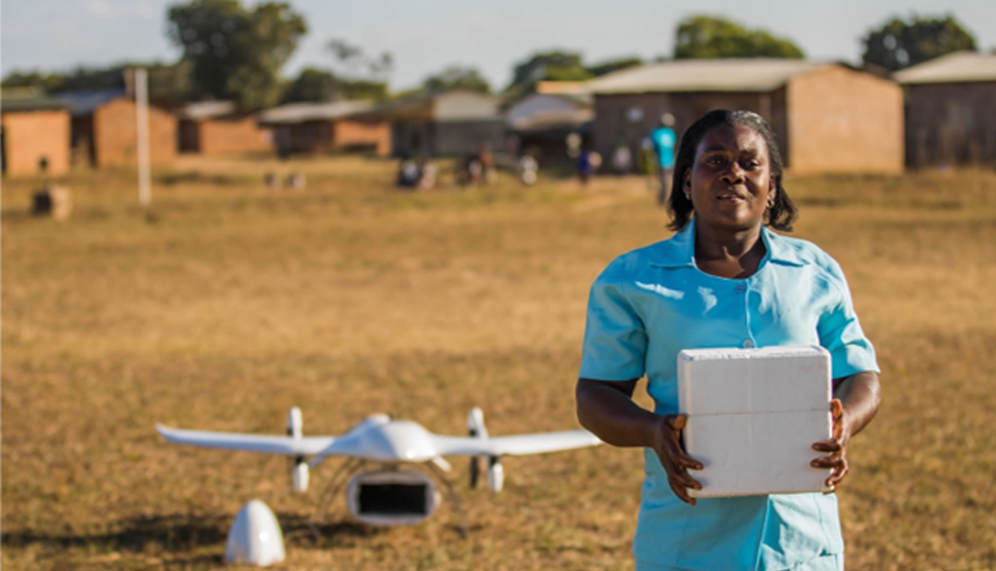 African nurse in front of a winged drone and hospital holding a cold box with medicine inside