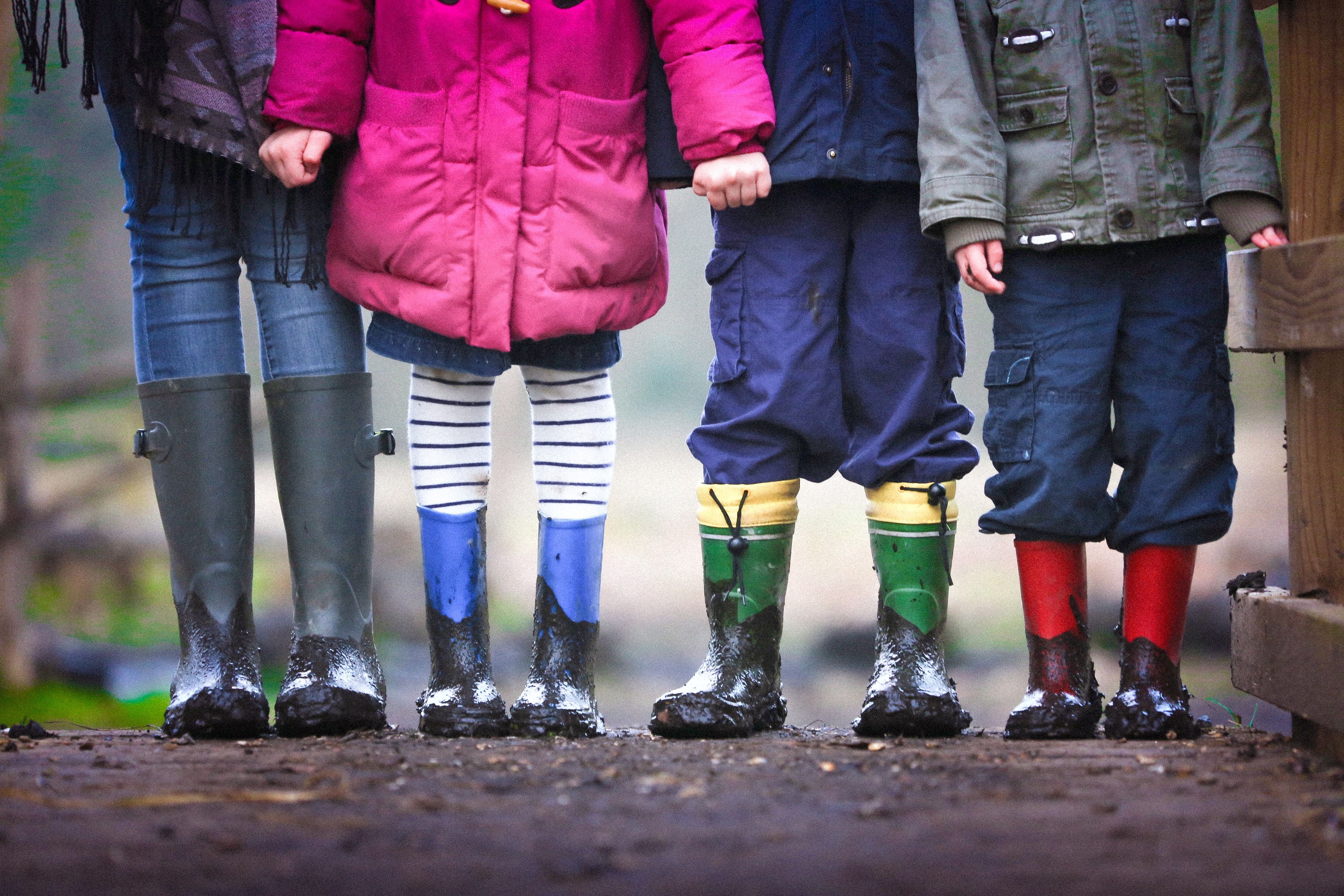 Four children stand together wearing boots covered with mud